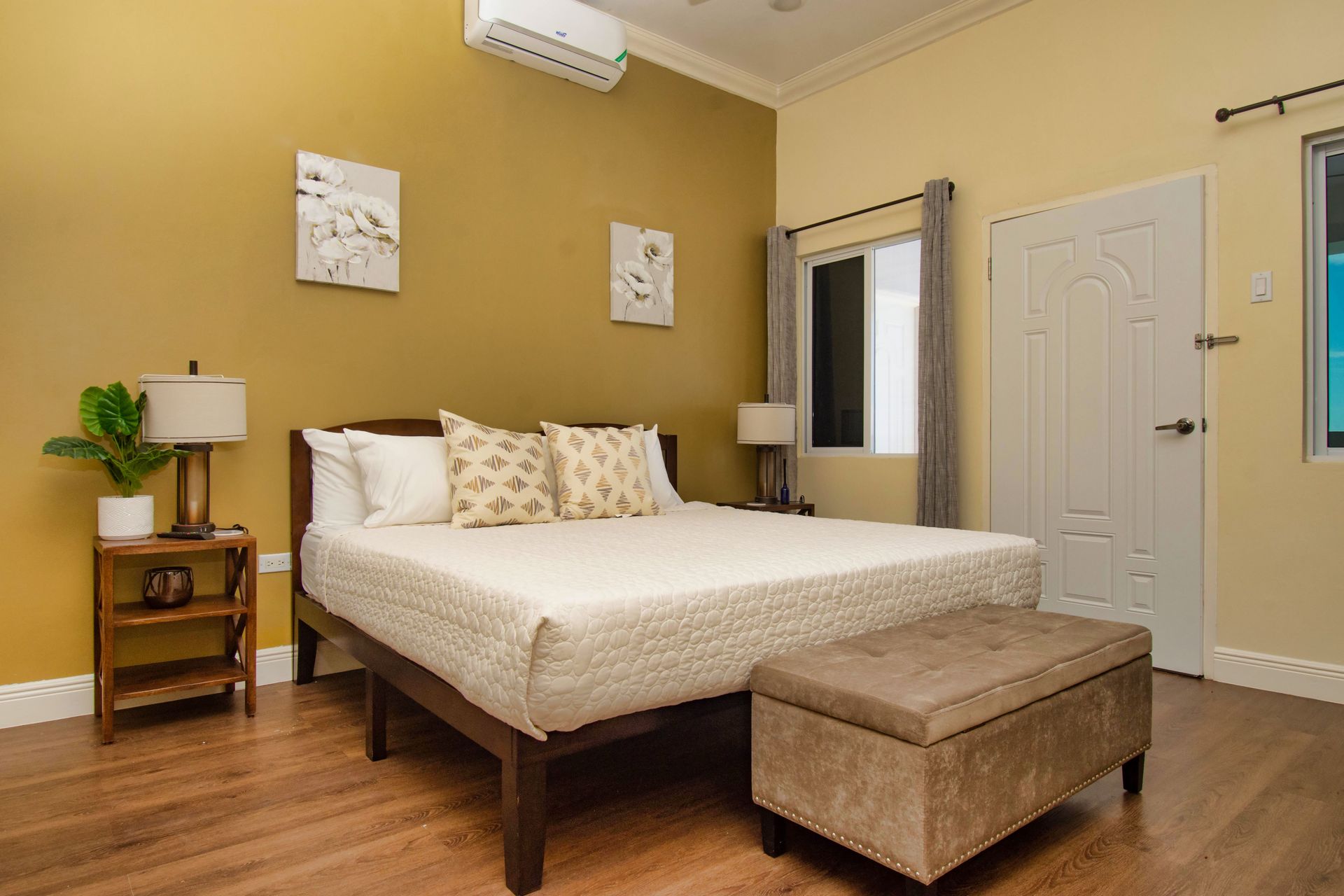 Bedroom with bed, ottoman, nightstands, and gold wall.