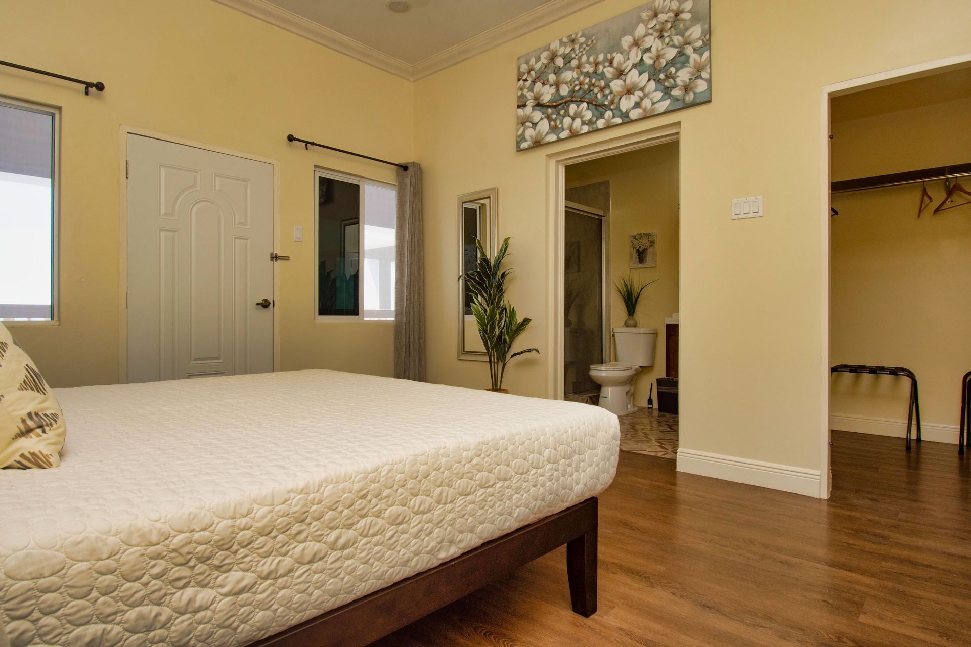 Bedroom with bed, doorway to bathroom, closet, and wall art. Yellow walls, wood floor.