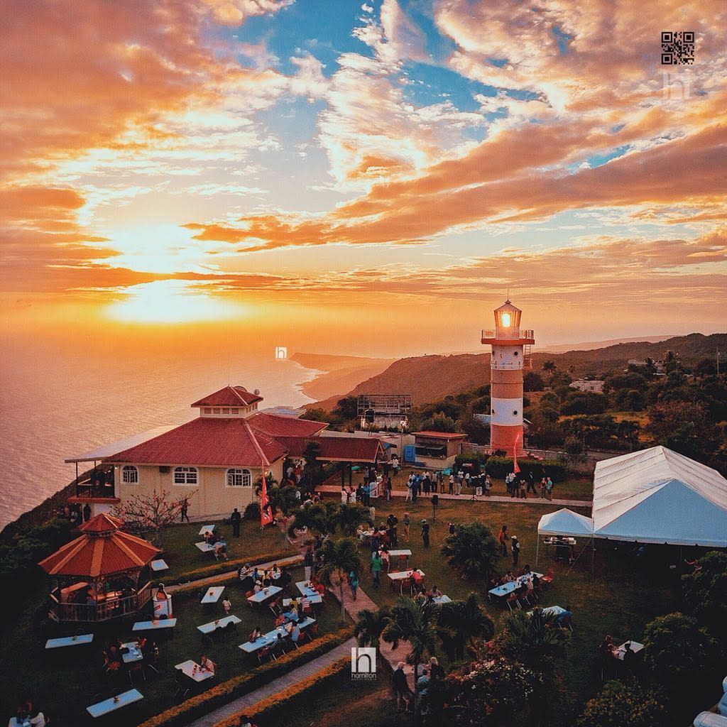 Sunset view of a coastal restaurant and lighthouse with people gathered, orange and white tower.