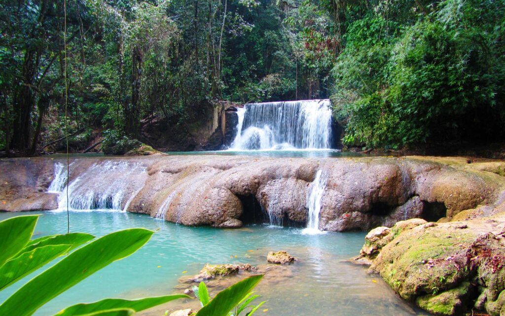 Waterfall cascading into a turquoise pool, surrounded by lush green vegetation.