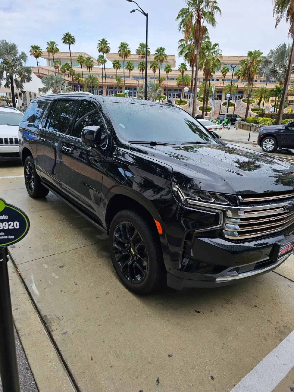 A black suv is parked in a parking lot with palm trees in the background.