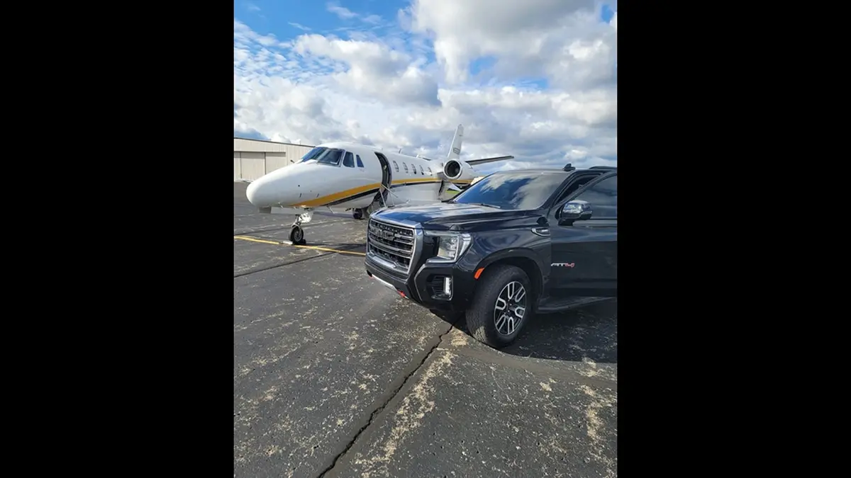 A car is parked next to a small plane at an airport.