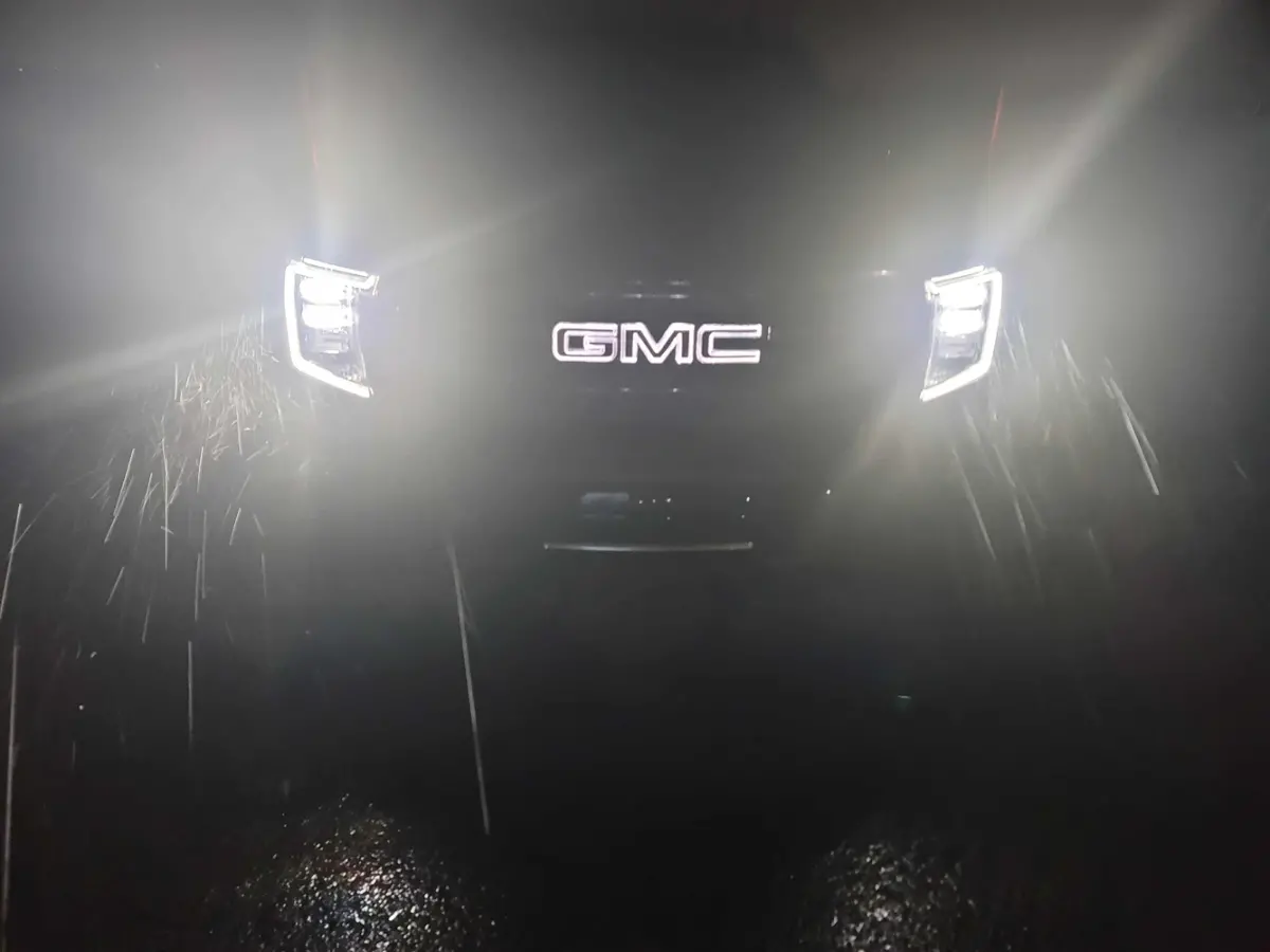 The headlights of a gmc truck are lit up in the dark.