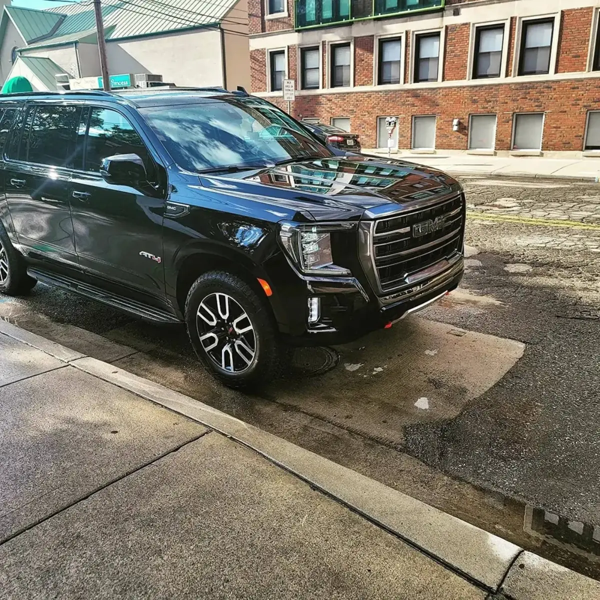 A black suv is parked on the side of the road in front of a brick building.