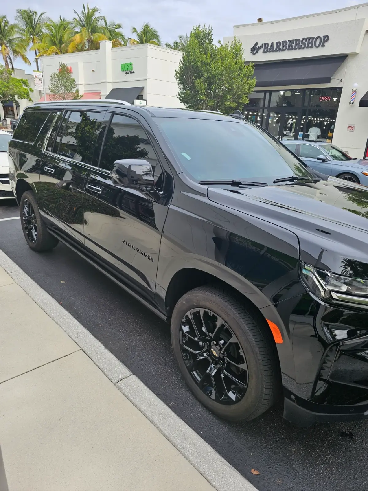 A black suv is parked on the side of the road in front of a store.