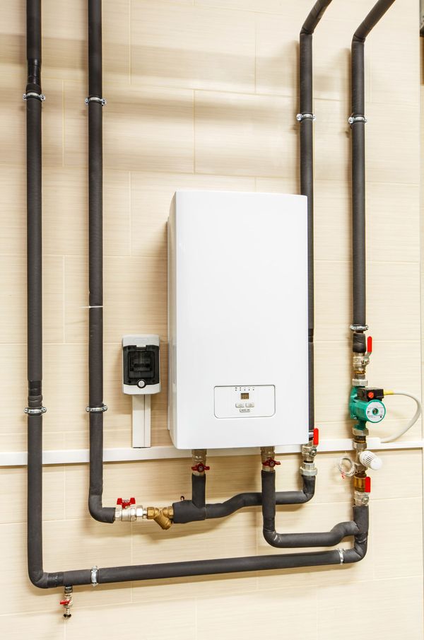 A white boiler is connected to a wall with pipes.