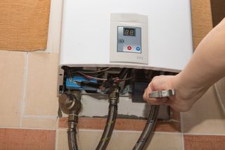 A person is fixing a water heater with a wrench.