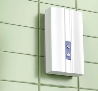 A white water heater is hanging on a green tiled wall.