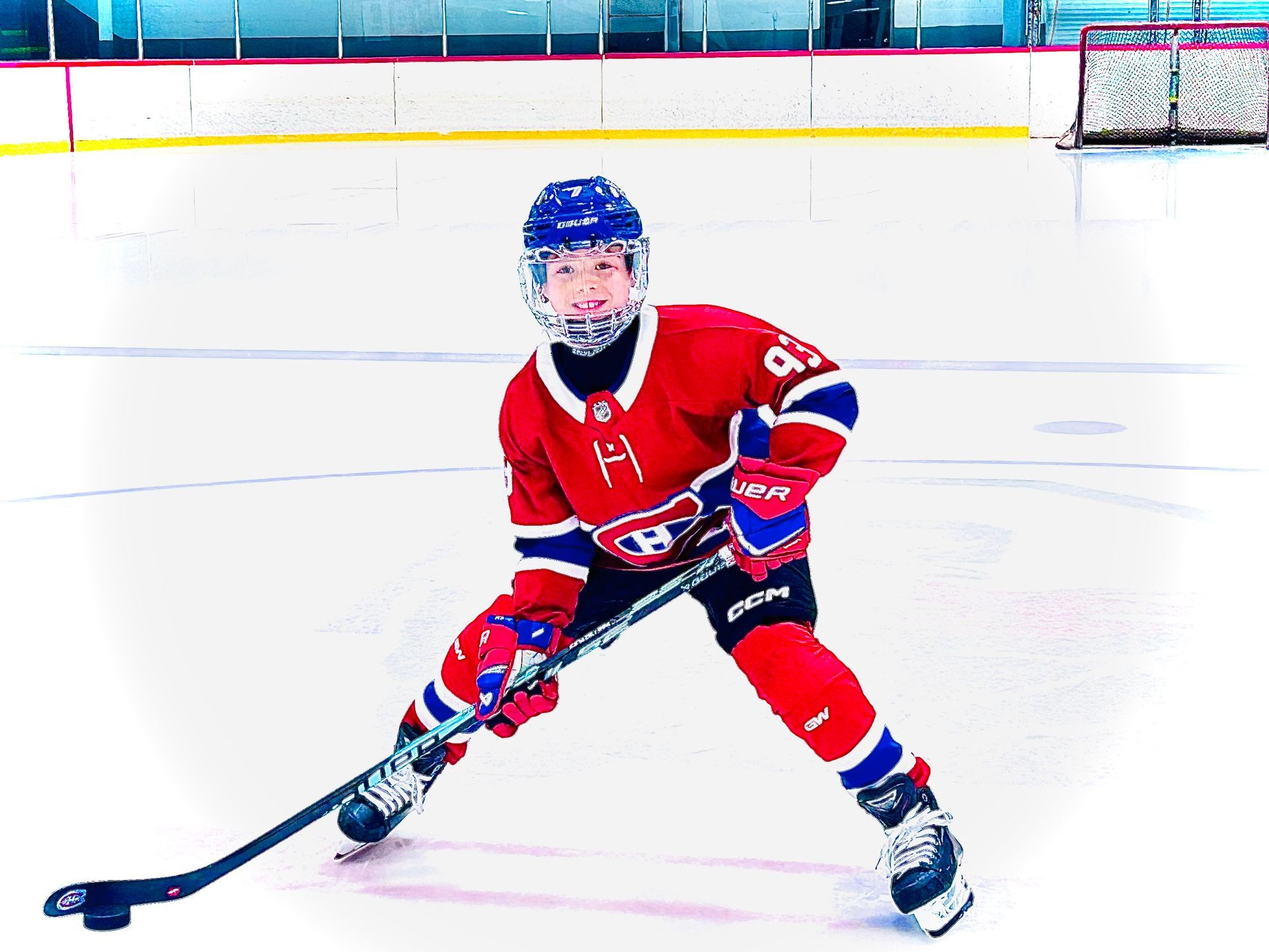 A smiling hockey player in a red Montreal Canadiens jersey and equipment stands on ice holding a stick, facing forward.