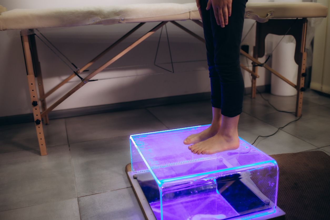A person meditates in a green shirt on a wooden deck with stairs in the background, framed by out-of-focus green leaves.
