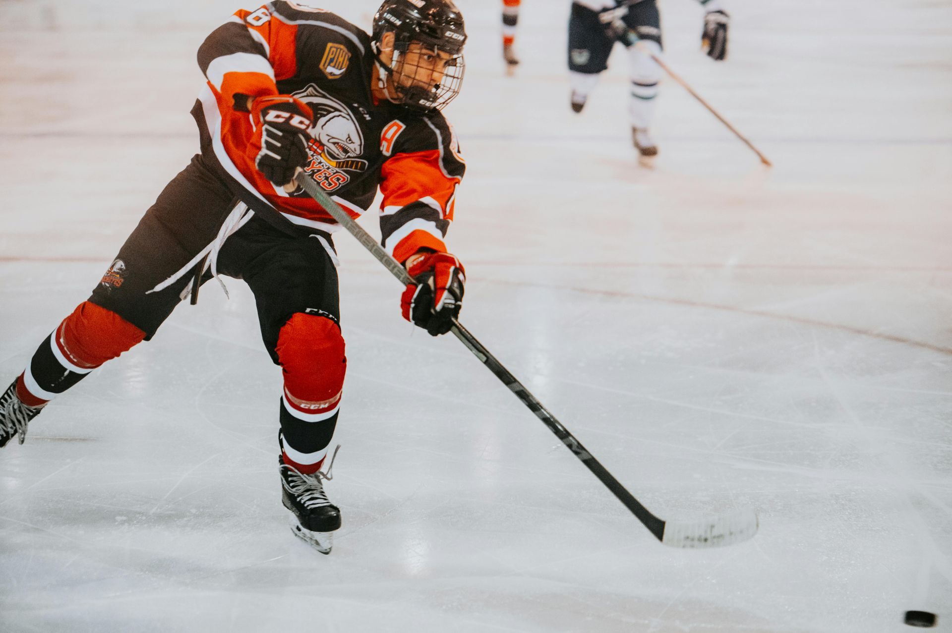Hockey player in red and black uniform shooting the puck on ice.