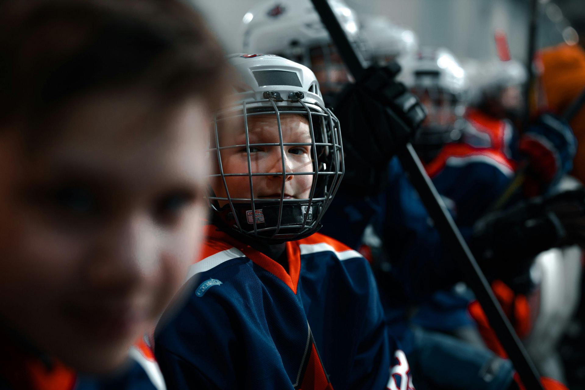 Hockey players in blue jerseys and helmets on bench, focused, waiting.