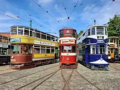 Vintage colorful double-decker trams parked on tracks under a blue sky, wires overhead.