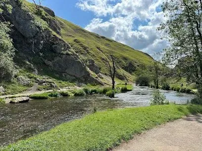 River flowing through a green, hilly landscape under a cloudy sky.