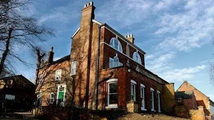 Brick building with arched windows, chimneys, and a green door under a blue sky with some trees.