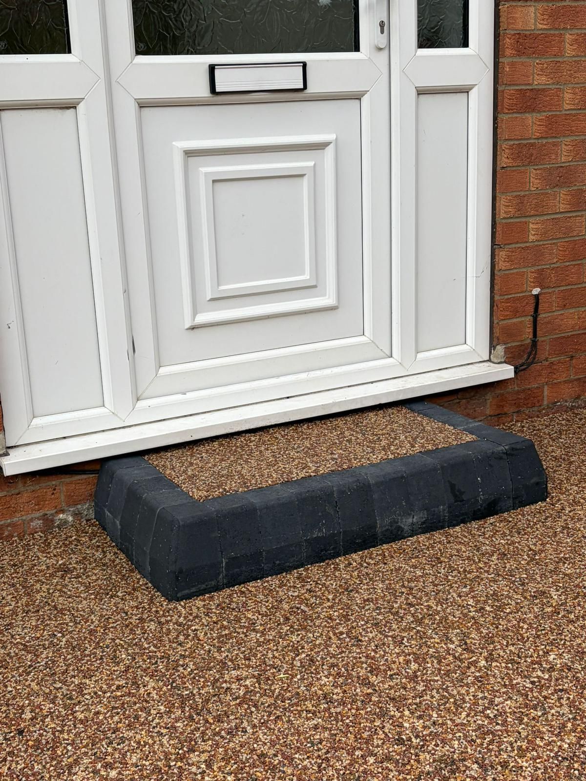 A white front door entrance with a dark-colored raised step filled with gravel, surrounded by a gravel driveway.