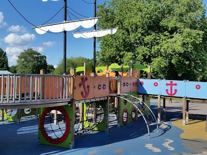 Playground with a ship-themed structure featuring sails, climbing nets, and colorful details.