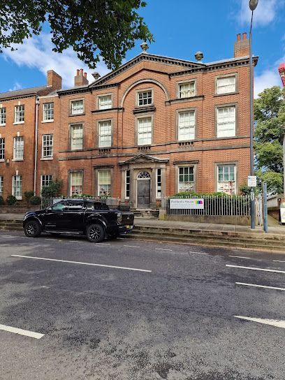 Brick building with symmetrical windows and a black SUV parked in front.
