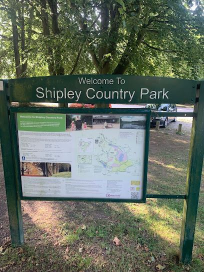 Sign welcoming visitors to Shipley Country Park. Green frame, map, and information panel. Trees and grass in background.