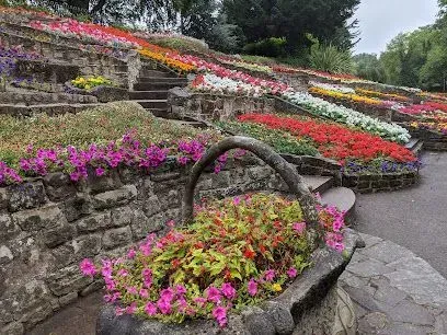 Flower-filled stone tiered garden with a basket of blooms in foreground, stairs leading upward, and diverse colorful flowers.