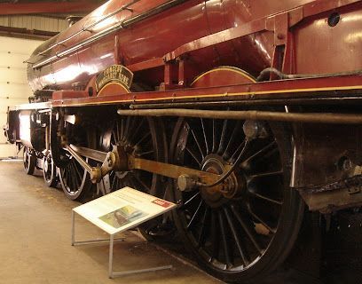 Red steam locomotive wheels and chassis in a museum, with information board.
