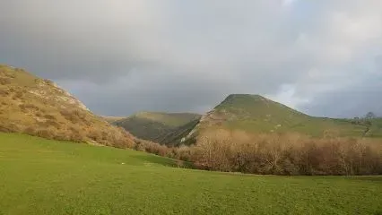 Green valley with rolling hills, a treeline, and cloudy sky.