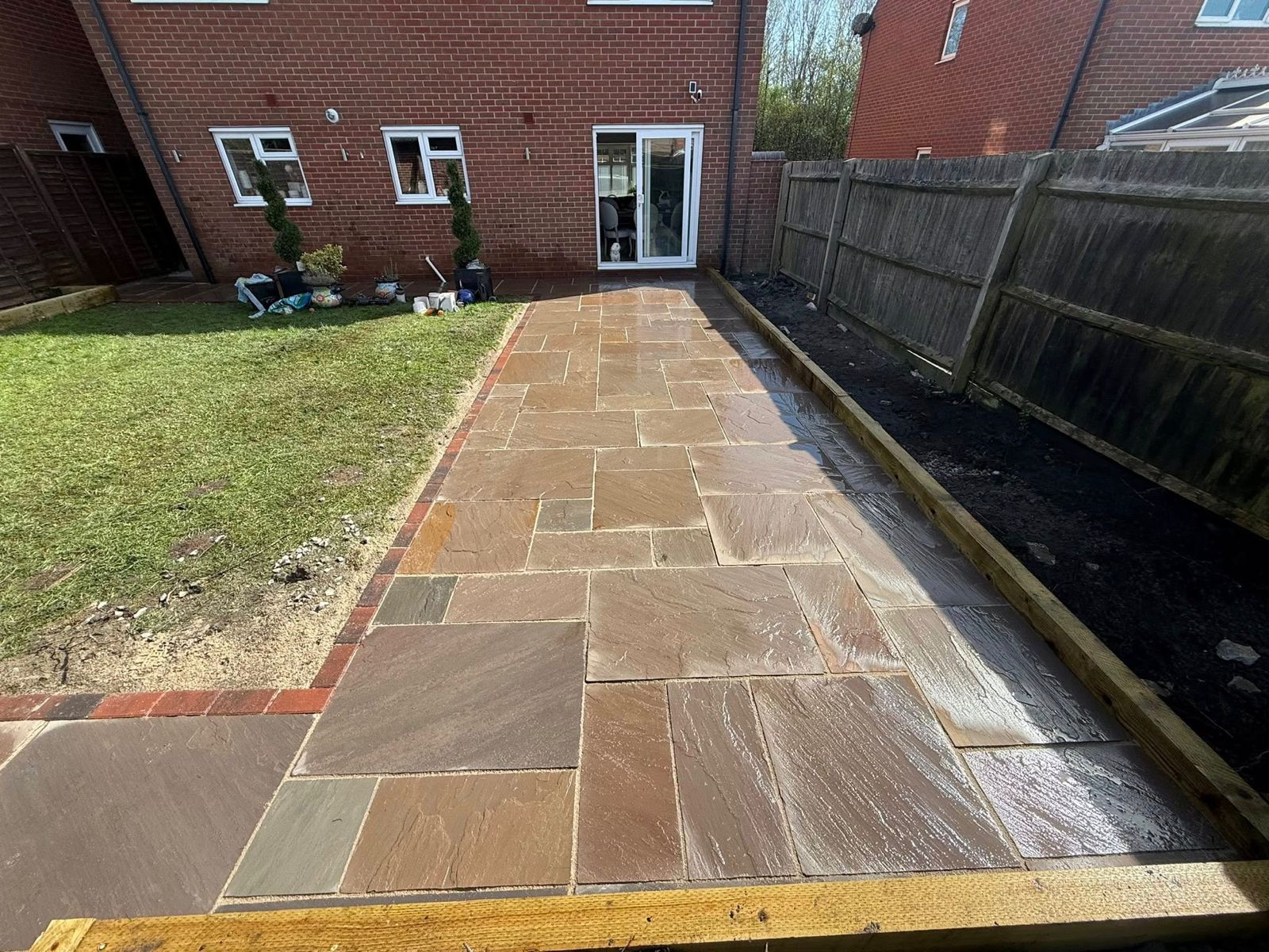 Stone path leading to a brick house back door, with lawn on the left and a fence on the right