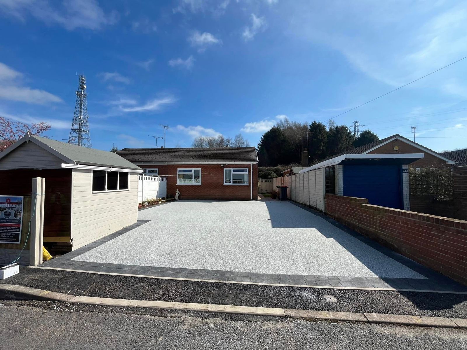 Gravel driveway between brick and white outbuildings under a blue sky