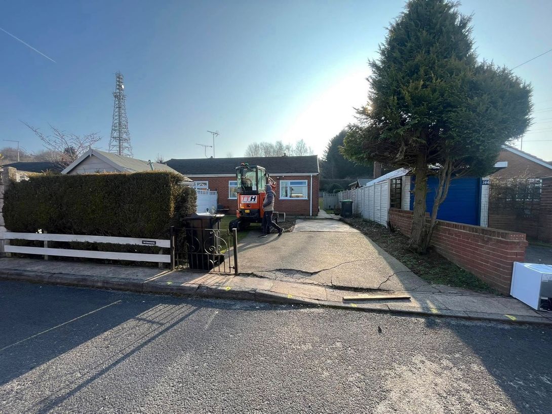 Aerial view of a two-story house with a gray roof and a green lawn, surrounded by trees and a driveway.