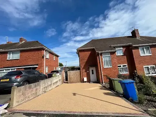 House with a gravel driveway, garage, and a stone building to the right on a sunny day.