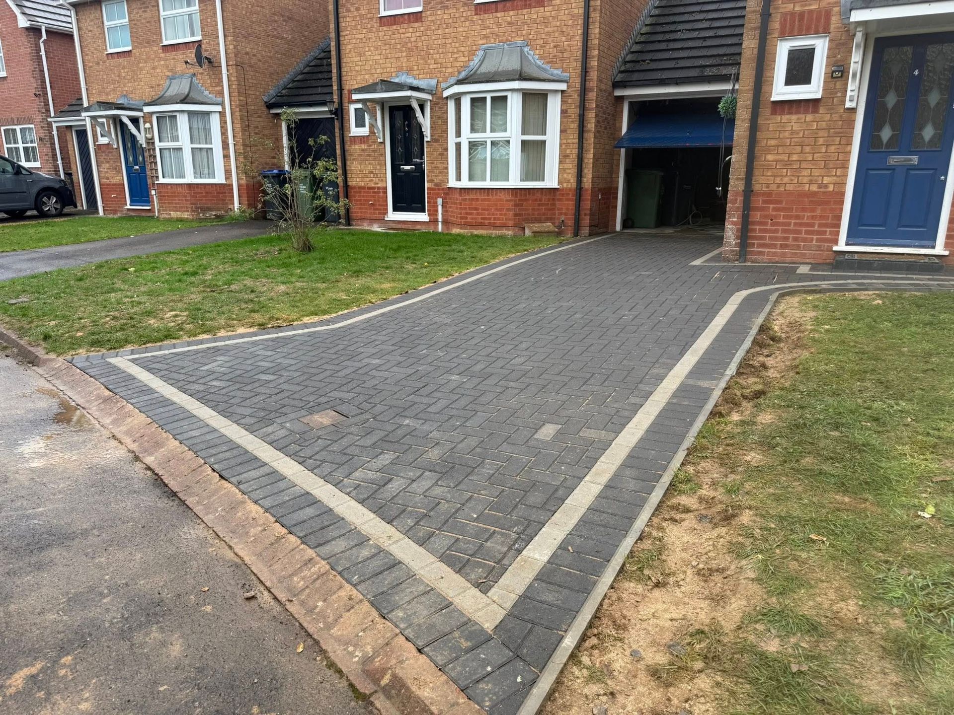 Dark gravel driveway curves past flowerbeds and houses on a sunny day.