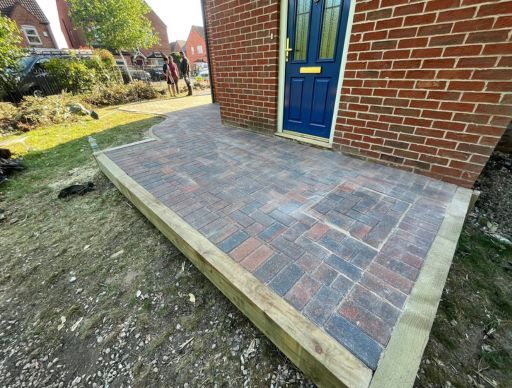 Driveway with brown gravel, black gate, white walls, steps, and green trash bin.