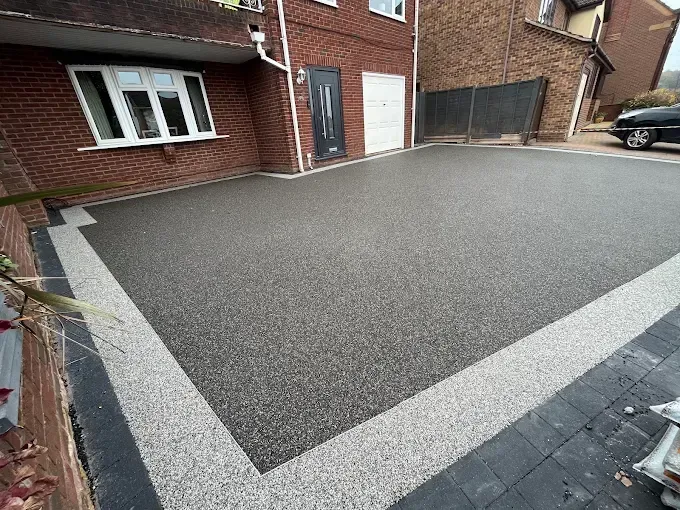 Dark grey resin driveway leading to a white garage door, flanked by gardens with greenery.