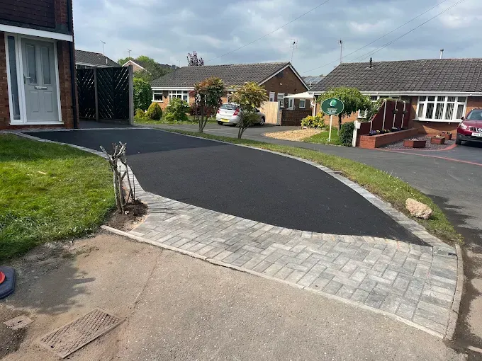 House with brown driveway and green lawn on a sunny day.
