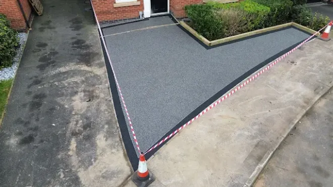 Dark grey resin driveway leading to a white garage door, flanked by gardens with greenery.