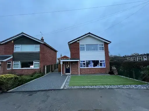 Red car parked next to a driveway made of gray gravel, leading to a brick house.