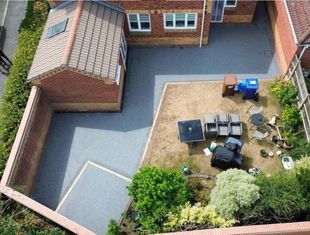 A gray resin patio with a table, chairs, and access to a house with a white door and windows.