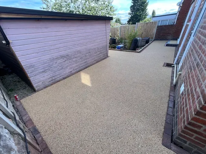 Aerial view of a two-story house with a resin driveway, green lawn, and surrounding trees.