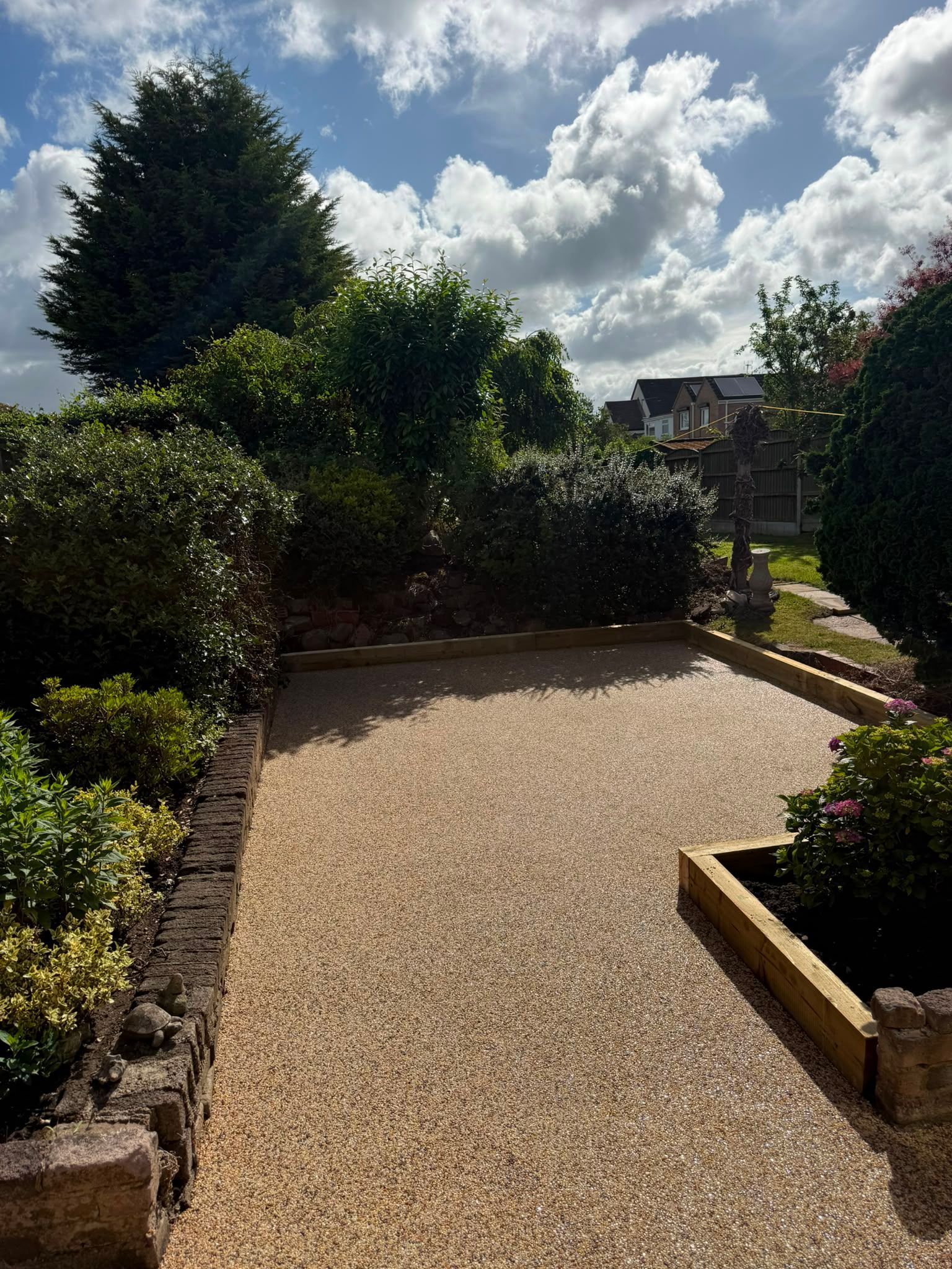Resin garden path bordered by shrubs and flowers under a bright, cloudy sky