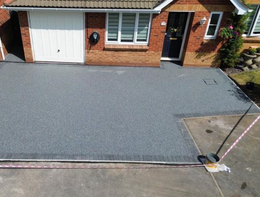 A house with resin driveway, brown fence, and real estate sign on the front lawn.