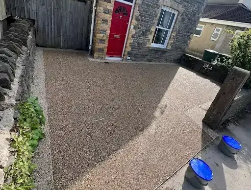 Driveway with brown gravel, black gate, white walls, steps, and green trash bin.