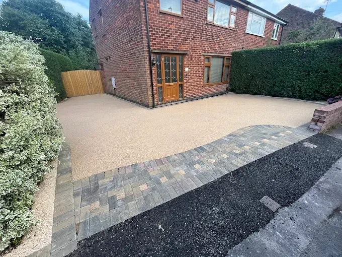 Resin courtyard between stone buildings, leading to a field under a cloudy sky.