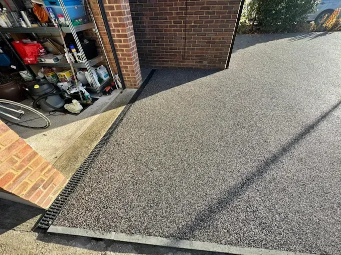 Outdoor resin patio with steps, coated in speckled gray aggregate. Glass doors of a white house in the background.