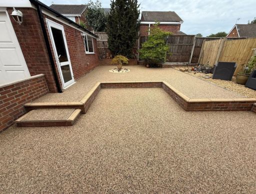 Resin bound driveway with light gravel, next to a low brick wall with potted plants.