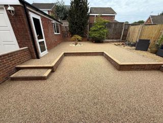 Resin bound driveway with light gravel, next to a low brick wall with potted plants.