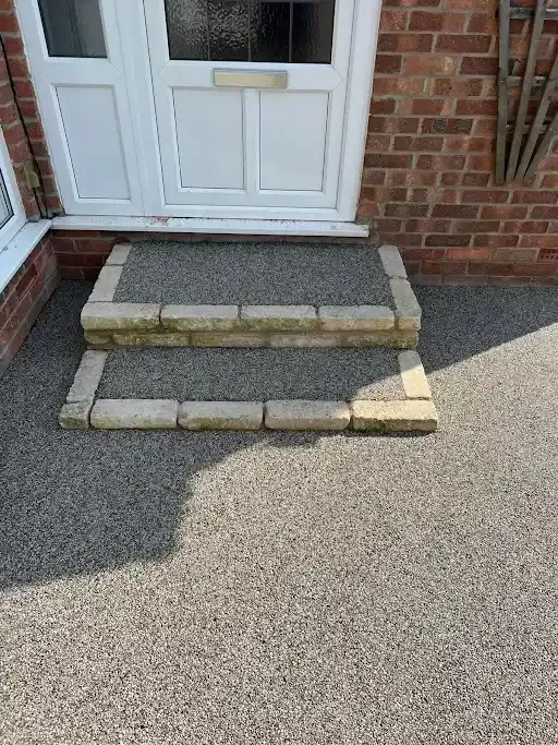 Dark gravel driveway curves past flowerbeds and houses on a sunny day.