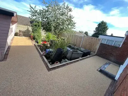 Shadow on a gravel driveway with a border of gray bricks, next to a building with white doors.