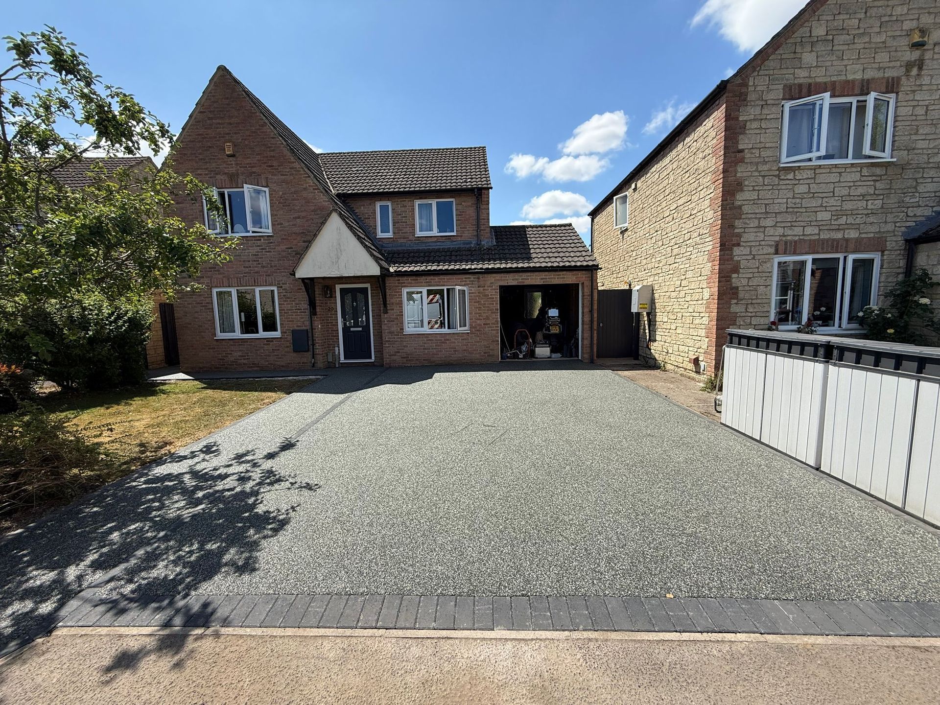 House with a gravel driveway, garage, and a stone building to the right on a sunny day.