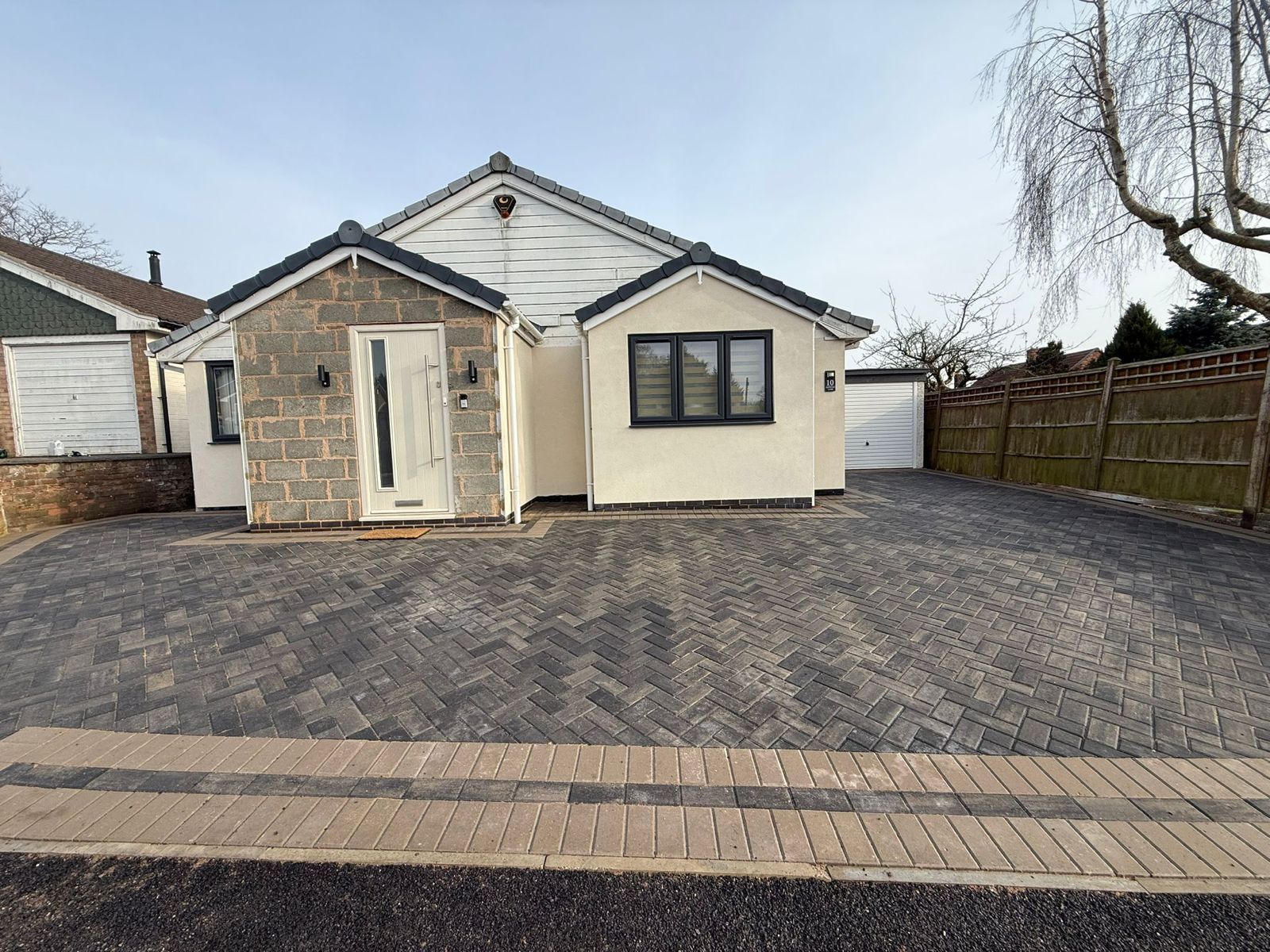 A single-story house with a stone-clad entrance and light-colored walls, featuring a paved driveway under a clear sky.