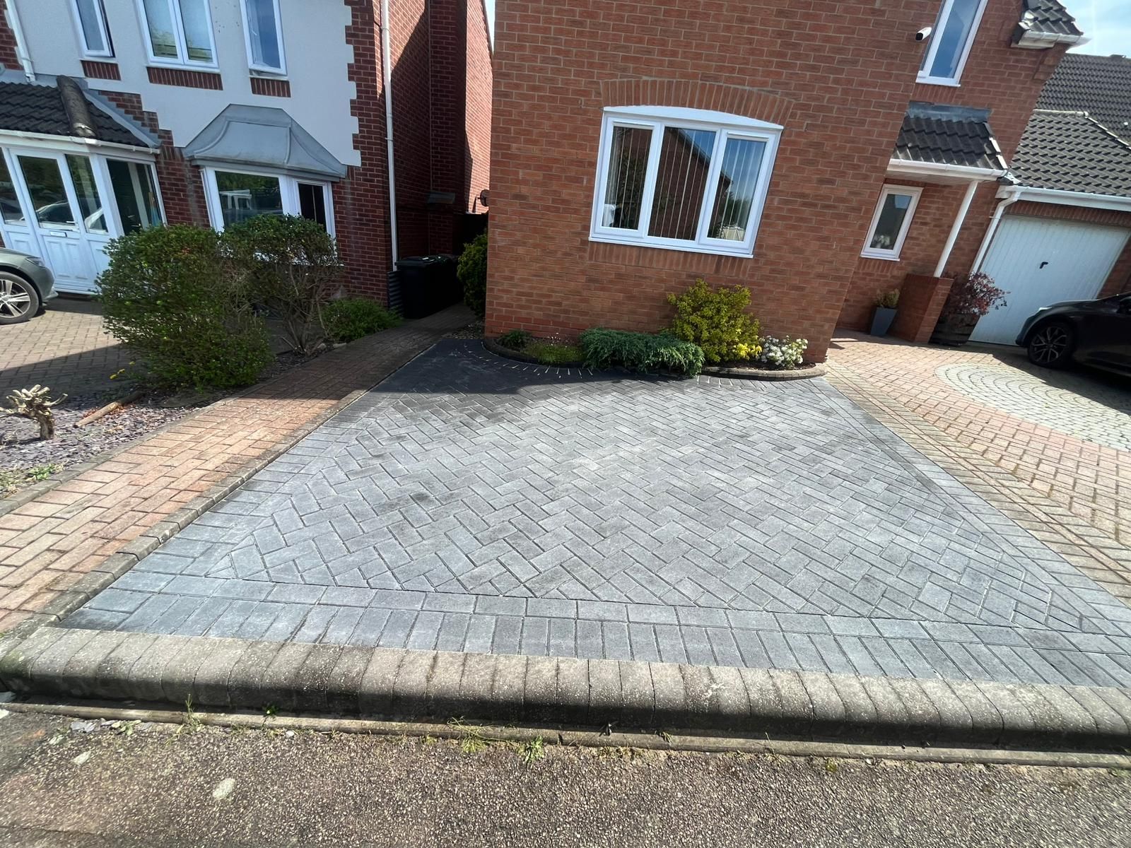 Brick driveway in front of a brick house with a white window.
